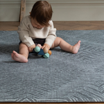 Baby girl plays with a wooden baby toy  supported on the eclipse monochrome play mat that provides protection from the cold floor