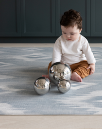 Baby playing with sensory metallic balls on Light blue and beige play mat with subtle diamond design inspired by ikat motifs ideal for family living spaces