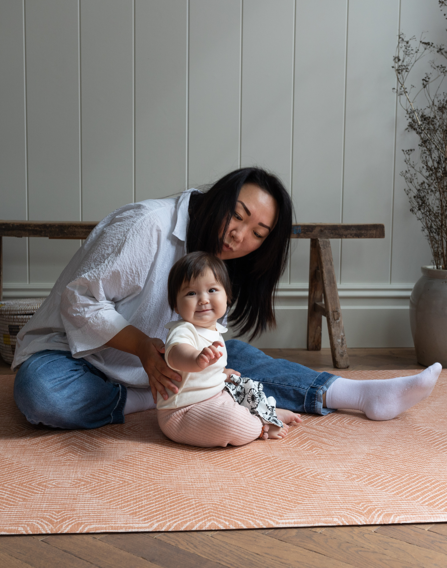 Baby and lady sit comfortably on thickly padded play mat with a modern kilim design 