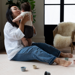 Lady holds baby sitting on pink foam baby mat making living more comfortable 