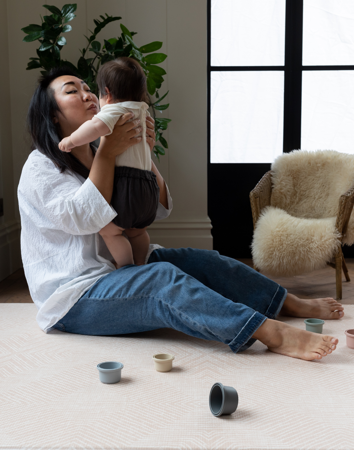 Lady holds baby sitting on pink foam baby mat making living more comfortable 