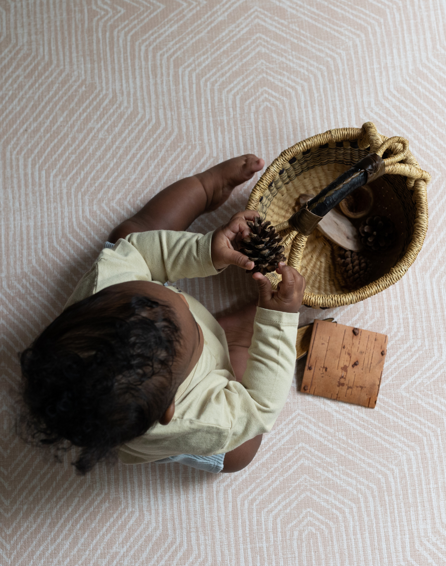 Little boy explores natural sensory basket for stimulation with thickly padded baby mat for a safe surface underneath 