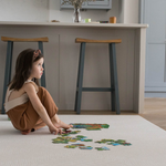 Child puts together a puzzle on the neutral Globe Trotter baby play mat that sits stylishly in a modern kitchen