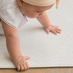 Little girl crawls across the Globe Trotter neutral play mat with a spongy surface that protects on hard wood flooring 