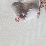 A baby lays on their back on the Globe Trotter play rug designed to look like a textile rug to keep your home stylish while providing comfort for babies on the floor