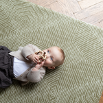 Baby is supported during play on the olive green play mat by Totter and Tumble with a decorative kilim effect 