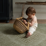 Baby plays with a basket sitting on the Harvester green baby mat that looks stylish in modern homes 