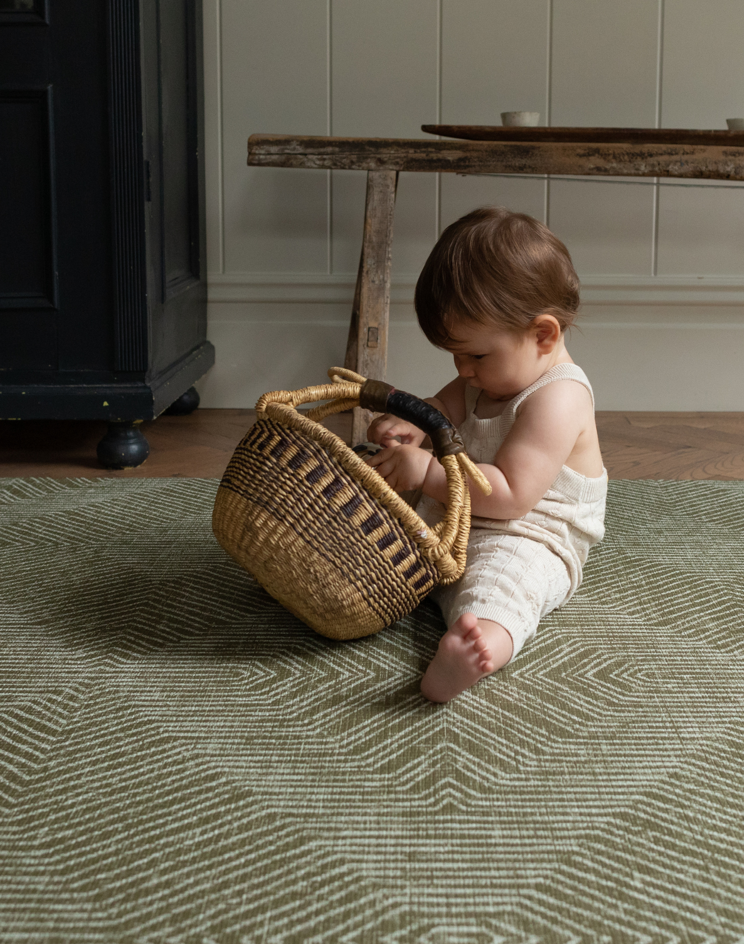 Baby plays with a basket sitting on the Harvester green baby mat that looks stylish in modern homes 