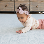 Baby with headband lays on protective play mat with modern scalloped design in gentle blue tones 