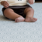 Baby sitting unaided on thick play mat with a modern scalloped design