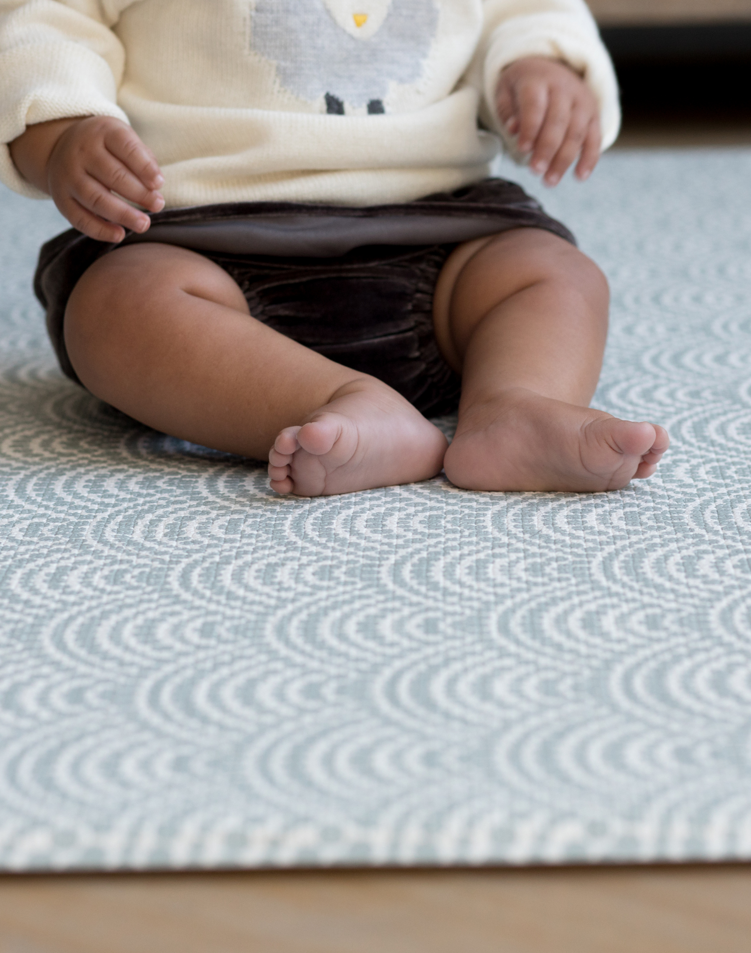 Baby sitting unaided on thick play mat with a modern scalloped design