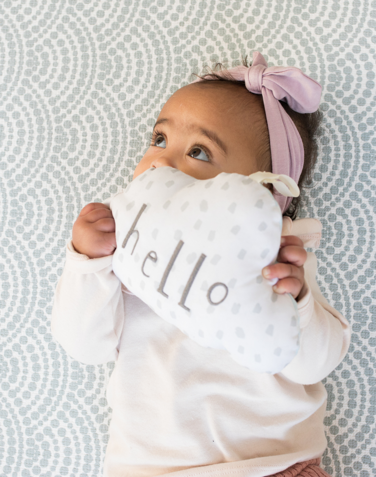 Baby resting on baby play mat with subtle scalloped pattern playing with soft toy 