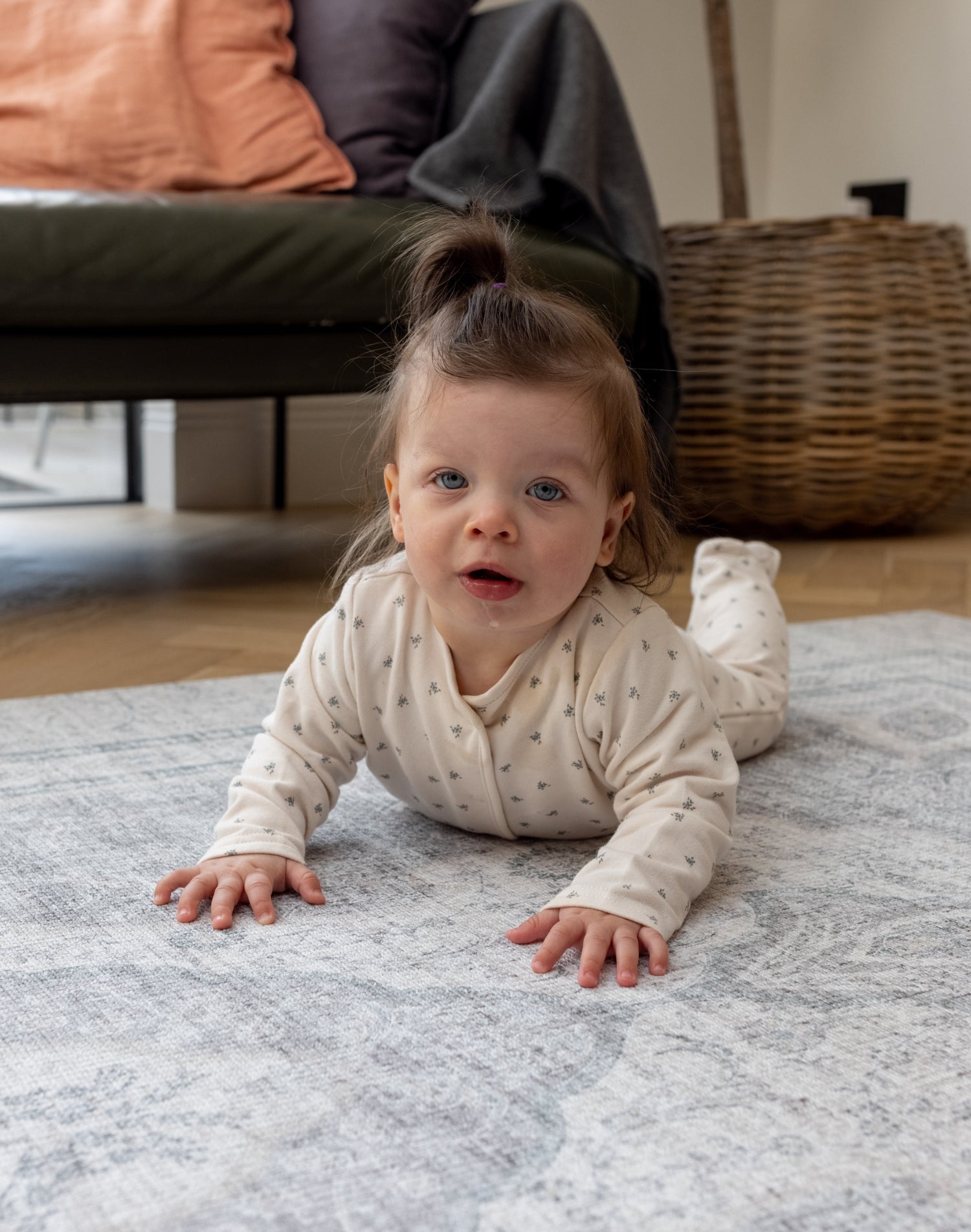 Baby crawls doing tummy time on a large waterproof play mat. The background is a family home interior space