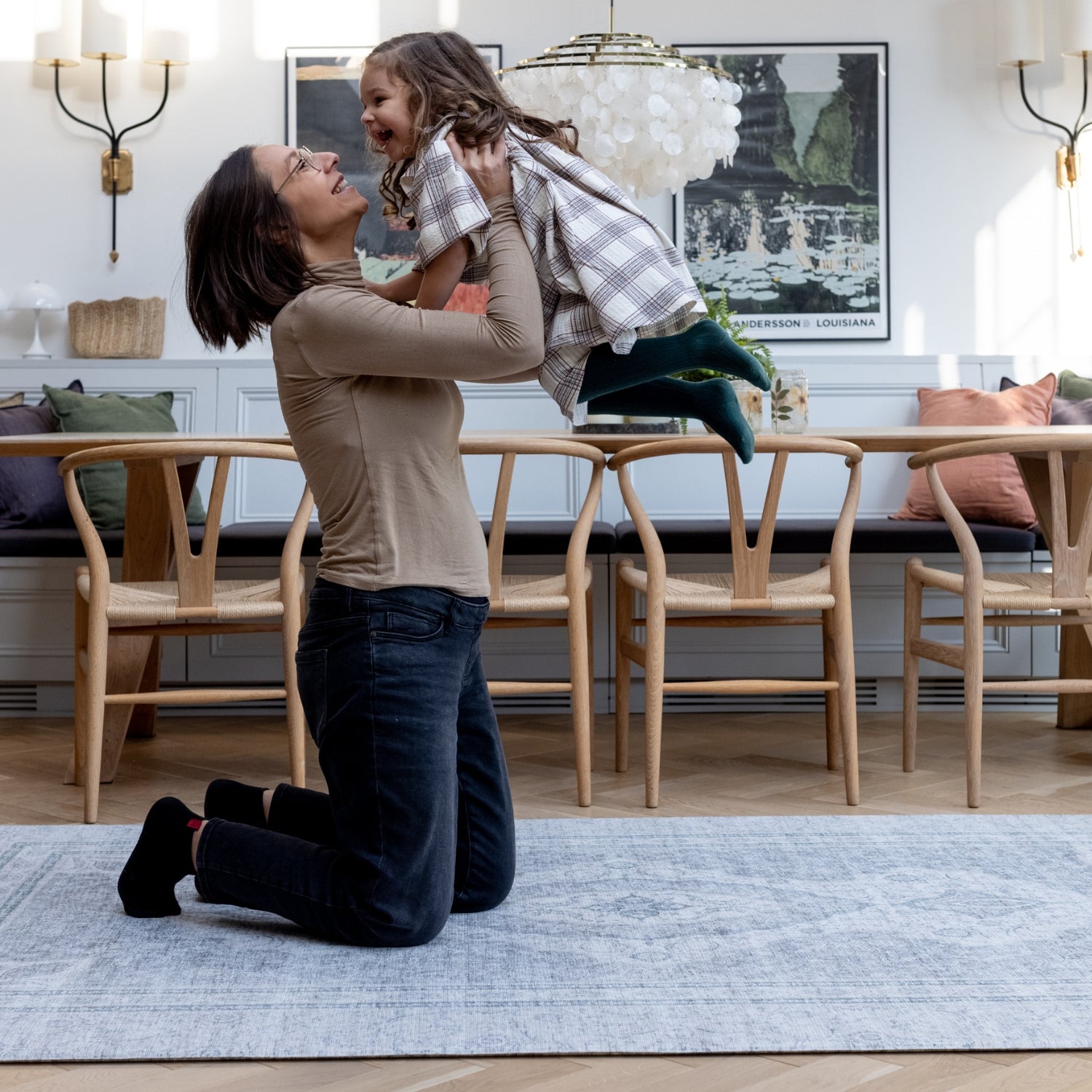 A mum lifts up her child while they play on a large floor mat for the living room. They are both smiling and laughing