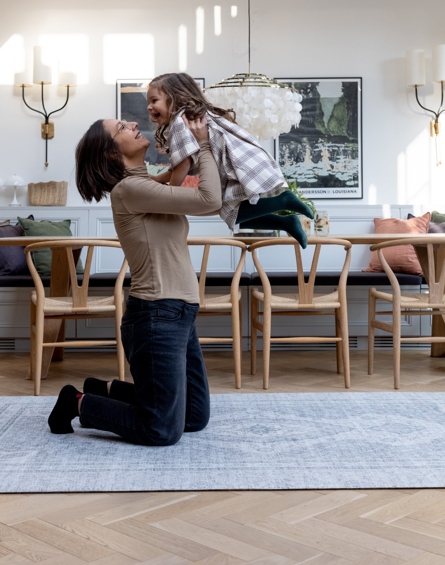 A mum lifts up her child while they play on a large floor mat for the living room. They are both smiling and laughing