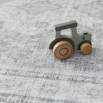 A wooden child's toy tractor lays on a big playmat for children. They playmat has an intricate Persian rug design