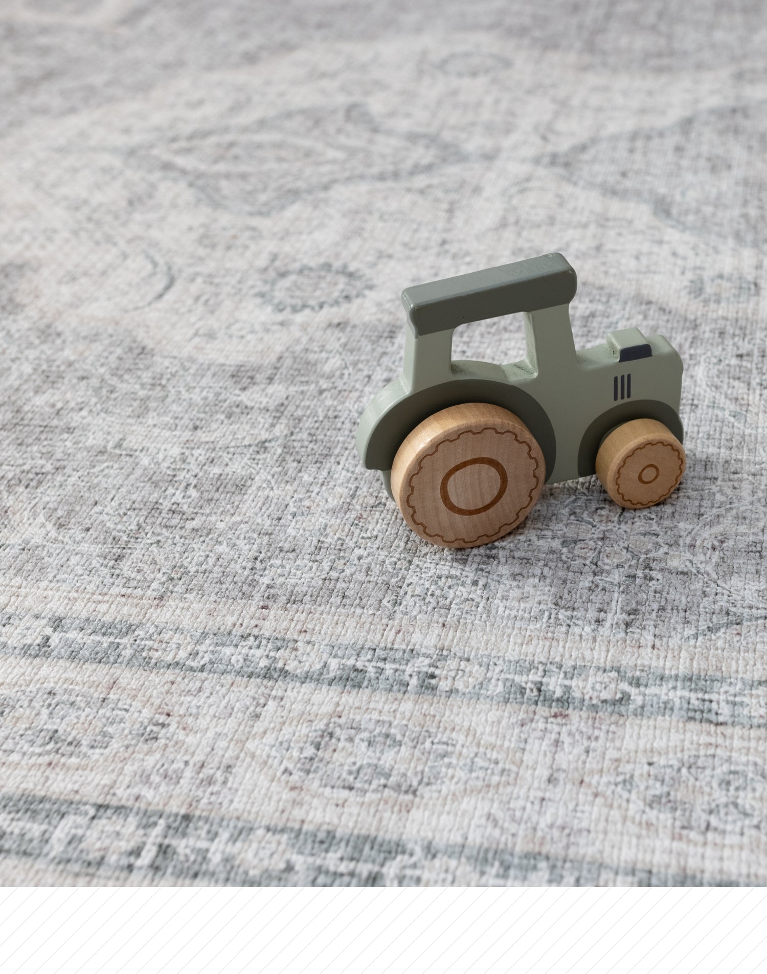 A wooden child's toy tractor lays on a big playmat for children. They playmat has an intricate Persian rug design