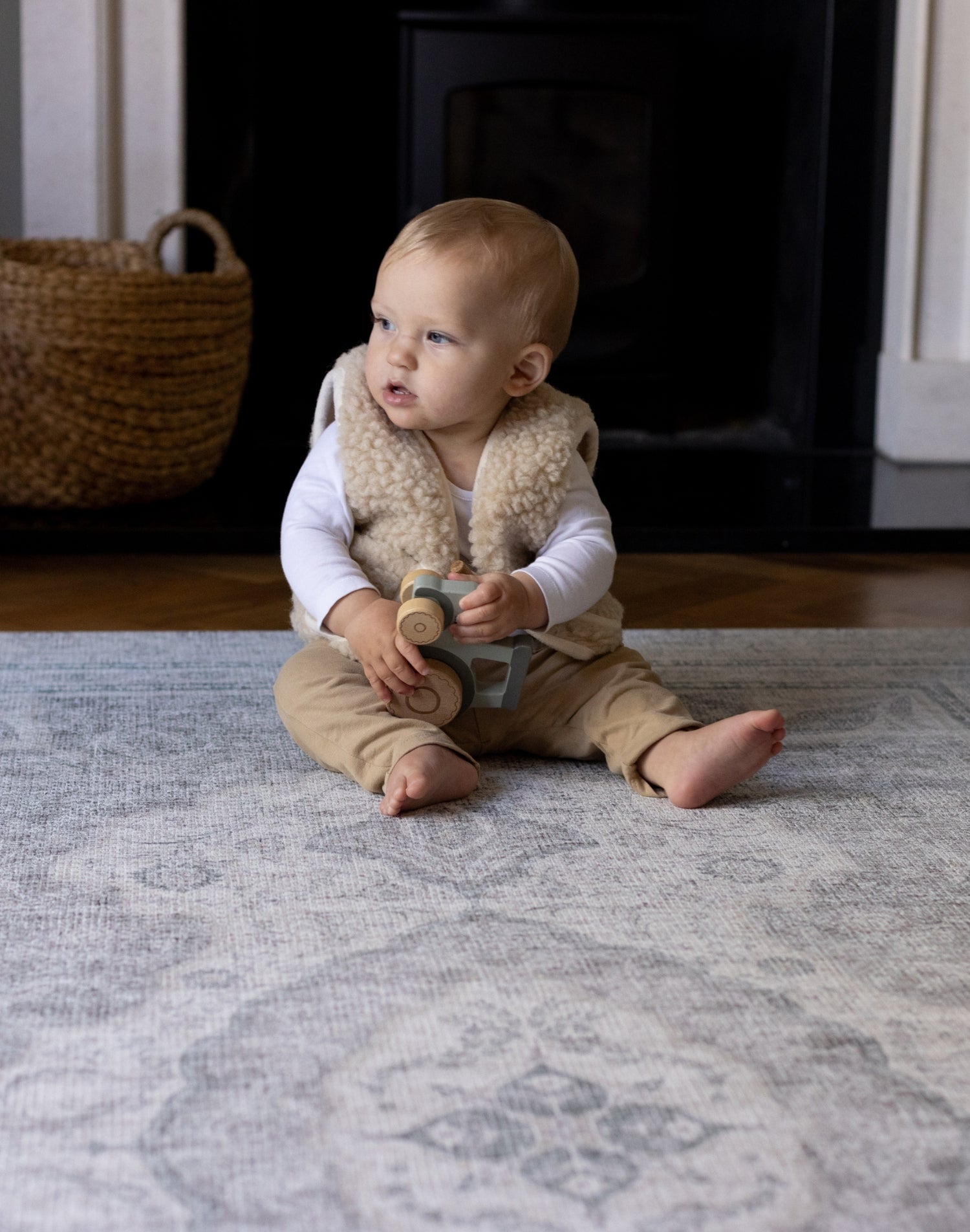 A baby sits up and is playing with a toy in the living room on a large playmat for infants