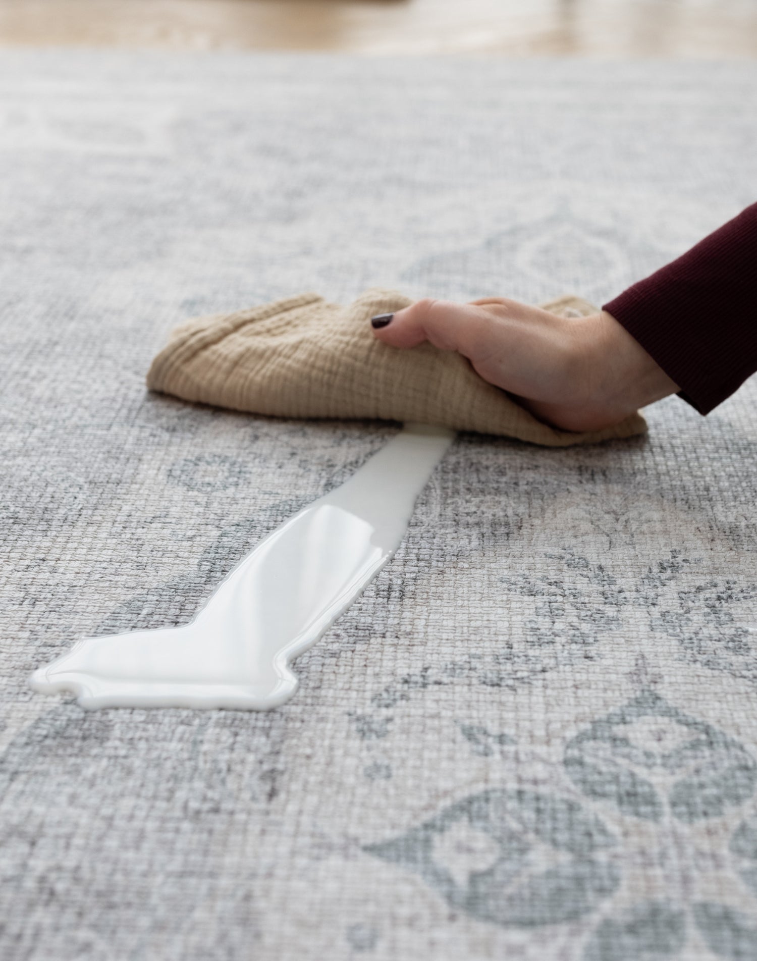 A hand cleans up a milk spillage with a soft cloth on large waterproof play mat