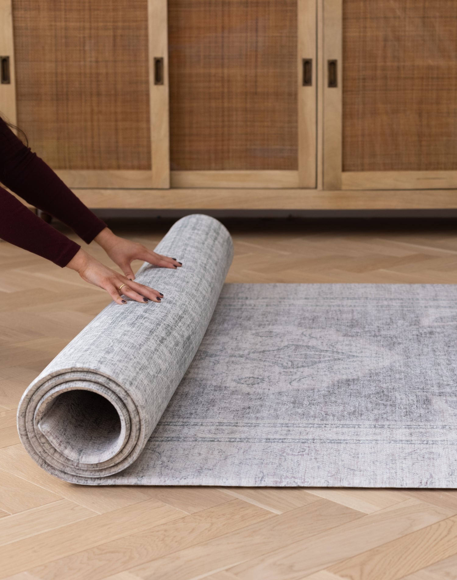 Hands roll out a rug-like large floor mat for babies that has two elegant designs on either side