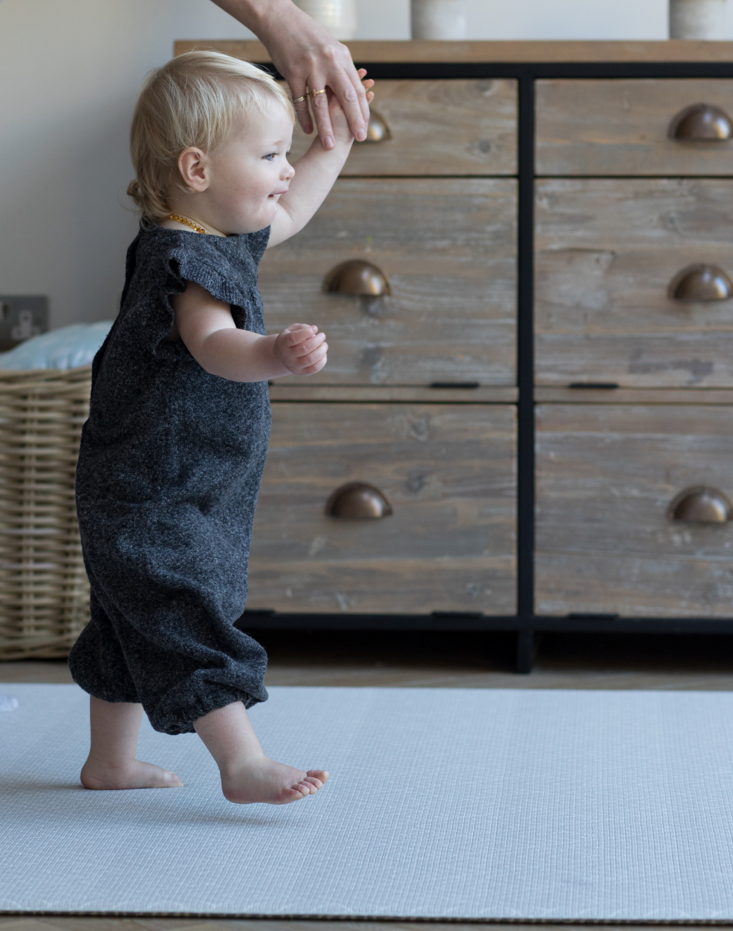 Toddler holds adults hand and walks across textured memory foam playmat 