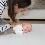 Mum rests gentle hand on the back of a baby laying on a supportive playmat with a gentle design ideal for modern spaces 