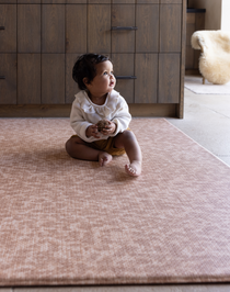 Baby sitting unaided on textured play mat thick memory foam design for support and protection on the floor soft orange play mat colour that blends seamlessly into modern family living spaces 