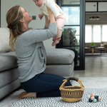 lady holds her baby while playing on the large round baby mat with a modern design 