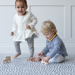 Toddlers play together on modern foam kids mat with a sensory motif