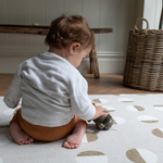 Little boy plays with wooden toy on beige baby play mat