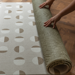 Hands unroll the double sided play mat with olive kilim and tan solstice designs perfect for play areas at home 