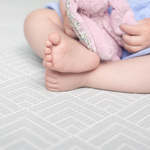 Baby sits safely on non toxic play mat designed from birth with a gentle grey design 